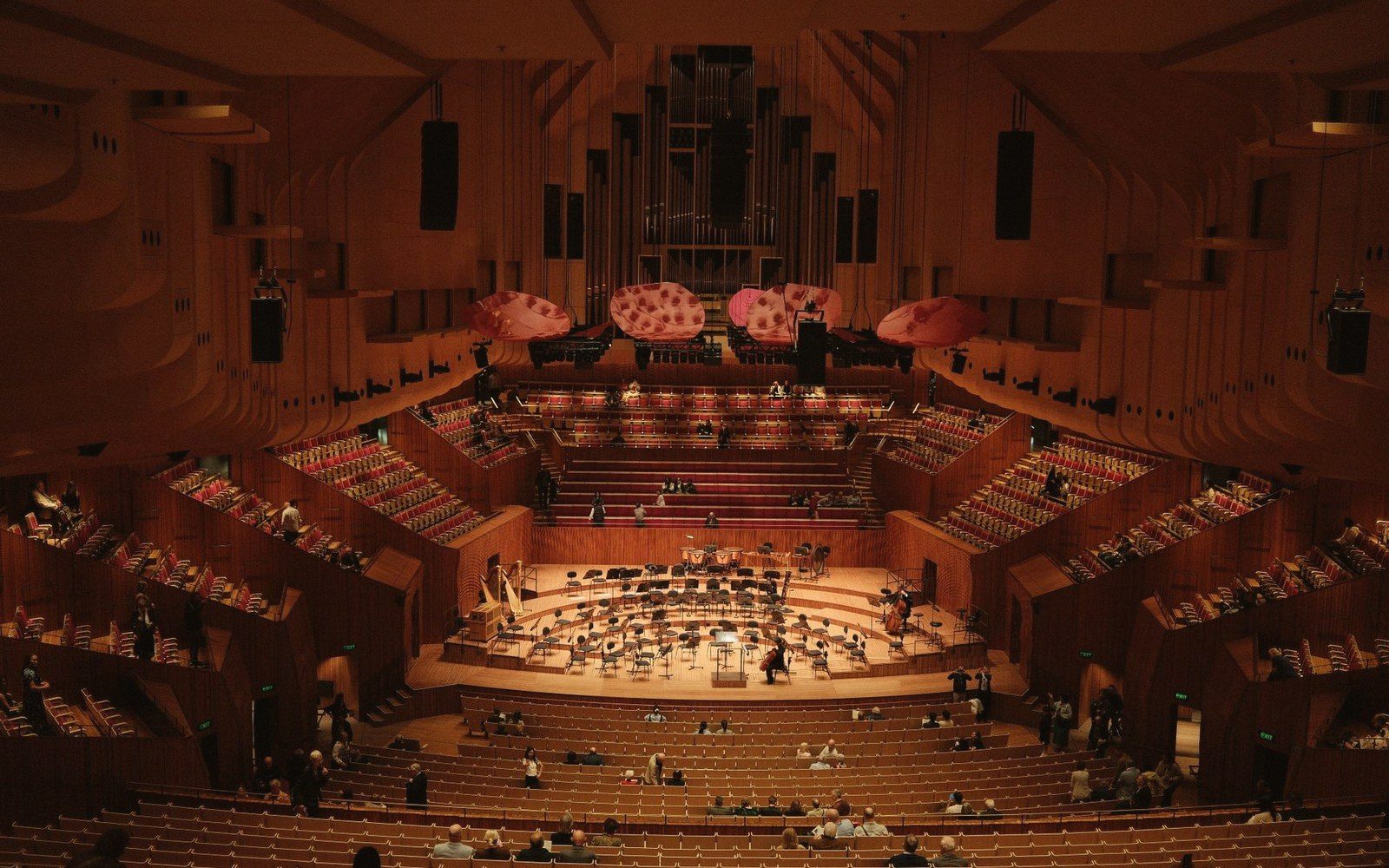 An opera house auditorium seen from the highest gallery, tiers of boxes curving below under low work light, stage curtain down