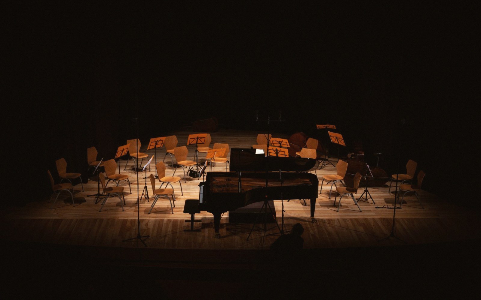 An empty orchestra pit seen from stage level, stands and chairs set but no musicians, conductor's podium unoccupied